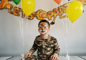 Chłopiec siedzi na tle fotograficznym i pozuje do zdjęcia wśród balonów.