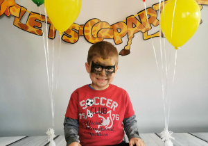 Chłopiec siedzi na tle fotograficznym i pozuje do zdjęcia wśród balonów.