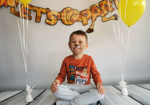 Chłopiec siedzi na tle fotograficznym i pozuje do zdjęcia wśród balonów