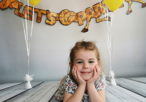 Dziewczynka leży na tle fotograficznym i pozuje do zdjęcia wśród balonów.