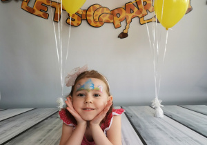 Dziewczynka leży na tle fotograficznym i pozuje do zdjęcia wśród balonów.