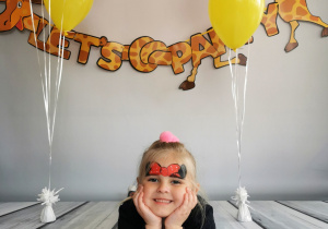 Dziewczynka leży na tle fotograficznym i pozuje do zdjęcia wśród balonów.