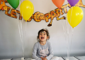 Dziewczynka siedzi na tle fotograficznym i pozuje do zdjęcia wśród balonów.
