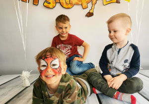 Trzech chłopców leży na tle fotograficznym i pozują do zdjęcia.