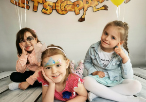 Trzy dziewczynki leżą na tle fotograficznym i pozując do zdjęcia.
