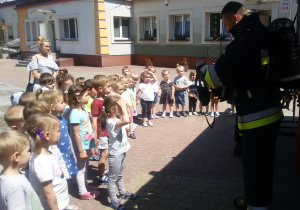 Widok na grupę dzieci i strażaka, który prezentuje im sprzęt strażacki.