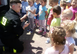Strażak prezentuje dzieciom strażacki radiotelefon.