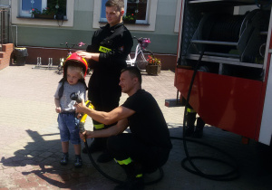 Widok na chłopca w hełmie strażackim i dwóch strażaków.