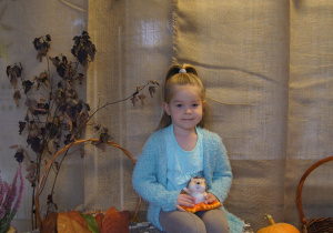 Dziewczynka pozuje do zdjęcia z jeżykiem na kolanach na jesiennym tle.