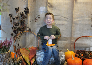 Chłopiec pozuje do zdjęcia z jeżykiem na kolanach na jesiennym tle.