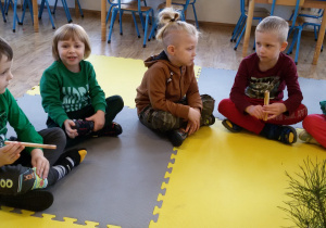 Widok na siedzące w półkolu dzieci, które oglądają kawałki drewna.