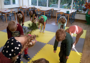 Widok na salę przedszkolną i dzieci naśladujące chore drzewa.