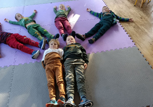 Chłopcy leżą na dywanie i układają kształt drzewa swoim ciałem.
