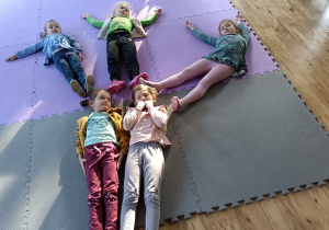 Dziewczynki leżą na dywanie i układają kształt drzewa swoim ciałem.