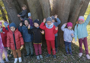 Dzieci pozują do zdjęcia. W tle widać konary drzew.