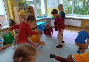 Dzieci podrzucają i zbierają opadające na podłogę kolorowe liście z papieru.