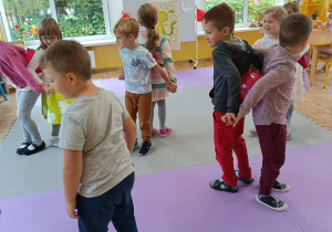 Dzieci tańczą w parach odwróceni do siebie tyłem. Między plecami umieszczony jest balon.