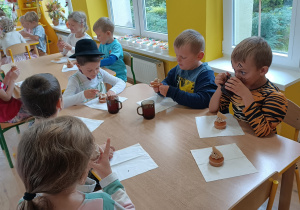 Dzieci siedzą przy stoliku i jedzą babeczki.