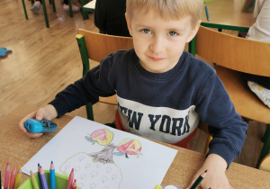 Chłopiec pozuje do zdjęcia robiąc pracę o jabłku.