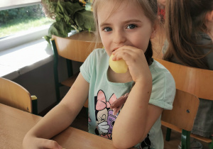 Dziewczynka pozuje do zdjęcia w dłoniach trzyma kawałki jabłka, które później zjada.