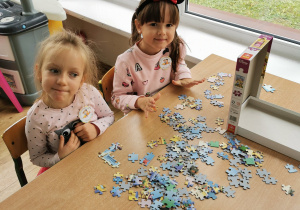 Dwie dziewczynki siedzą przy stole i układają puzzle.