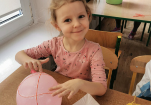 Dziewczynka siedzi przy stole i owija balon włóczką tworząc dynie.