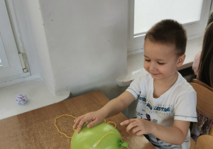 Chłopiec siedzi przy stole i owija balon włóczką tworząc dynie.