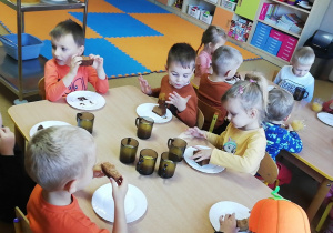 Grupa dzieci pije sok pomarańczowy i je ciasto dyniowe.
