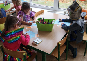 Dzieci wykonują przy stoliku pracę plastyczną.