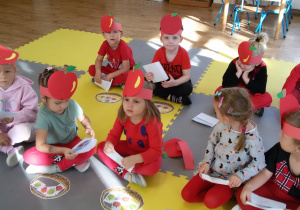 Widok na siedzące w dwóch rzędach dzieci. Przed nimi leżą papierowe koszyczki z jabłkami.
