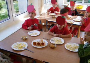 Widok na siedzące przy stolikach dzieci. Na stolikach stoja talerze z drobno pokrojonymi jabłkami oraz talerz z waflowymi rożkami.
