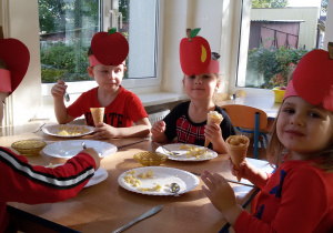 Widok na czworo siedzących przy stoliku dzieci, które przygotowuja deser z jabłek.