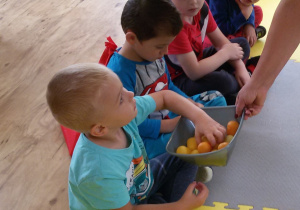 Widok na 4 chłopców siedzących na piankowych puzzlach. Oluś sięga ręką do miseczki z pomarańczowymi jajeczkami.