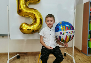 Chłopiec pozuje do zdjęcia trzymając balon urodzinowy.