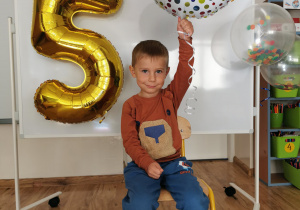 Chłopiec pozuje do zdjęcia trzymając balon urodzinowy.