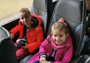 Dwoje uśmiechniętych dzieci pozują do zdjęcia siedząc w autokarze.