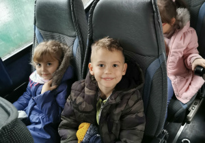 Uśmiechnięte dzieci pozują do zdjęcia siedząc w autokarze.