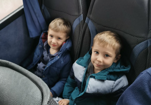 Uśmiechnięte dzieci pozują do zdjęcia siedząc w autokarze.