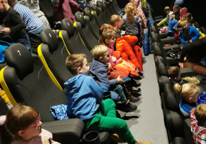 Grupa dzieci siedzi w sali kinowej czekając na seans.