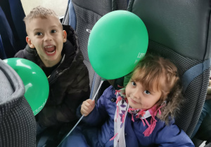Dwoje dzieci pozuje z balonami do zdjęcia siedząc w autokarze.