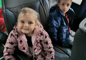 Dwoje dzieci pozuje z balonami do zdjęcia siedząc w autokarze.