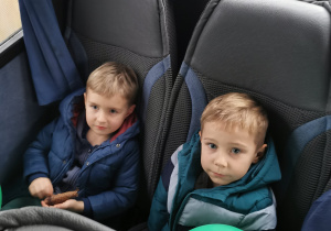 Dwóch chłopców pozuje z balonami do zdjęcia siedząc w autokarze.
