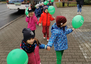 Zadowolone dzieci trzymając w dłoniach balony idą w stronę przedszkola po zakończonej wycieczce autokarowej do kina w Pabianicach.