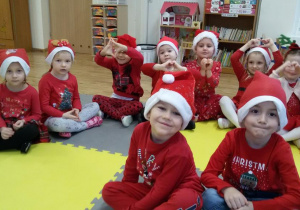 Widok na grupę 9 dzieci w czerwonych strojach i „mikołajkowych czapeczkach”.