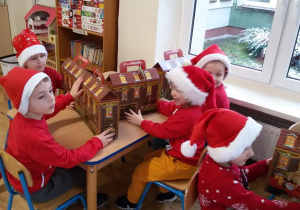 Widok na 5 chłopców siedzących przy dwóch stolikach, na których stoją pudełka domki- prezenty od Świętego Mikołaja.