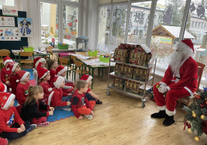 Dzieci siedzą na macie i rozmawiają z Mikołajem.