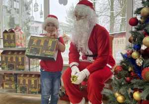 Chłopiec pozuje do zdjęcia ze Świętym Mikołajem trzymając w rękach prezent.