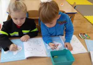 Jakub i Marcel wykonują zadania w książeczkach.