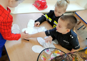 Widok na trzech siedzących przy stoliku chłopców, którzy podświetlają obrazki latarką.