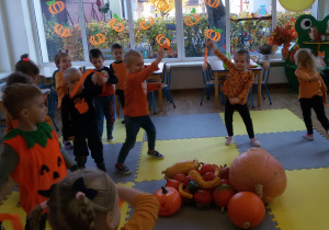 Widok na grupę przedszkolaków tańczących z pomarańczowymi wstążkami.